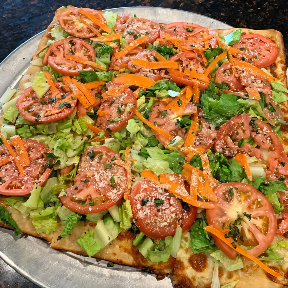 Via Roma Pizza's square pizza topped with fresh lettuce, sliced tomatoes, shredded carrots, and parmesan cheese.