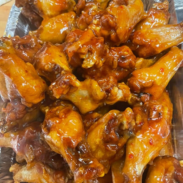 Close-up of a foil container filled with numerous glistening, saucy chicken wings from Via Roma Pizza.