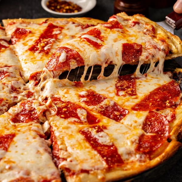 A slice of Via Roma pepperoni pizza being lifted, showing melted cheese stretching.