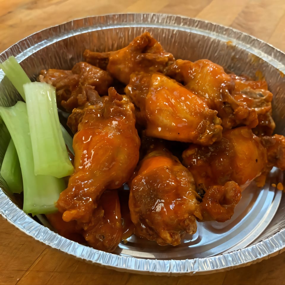 Via Roma Pizza's buffalo wings and celery sticks in a foil container on a wooden table.